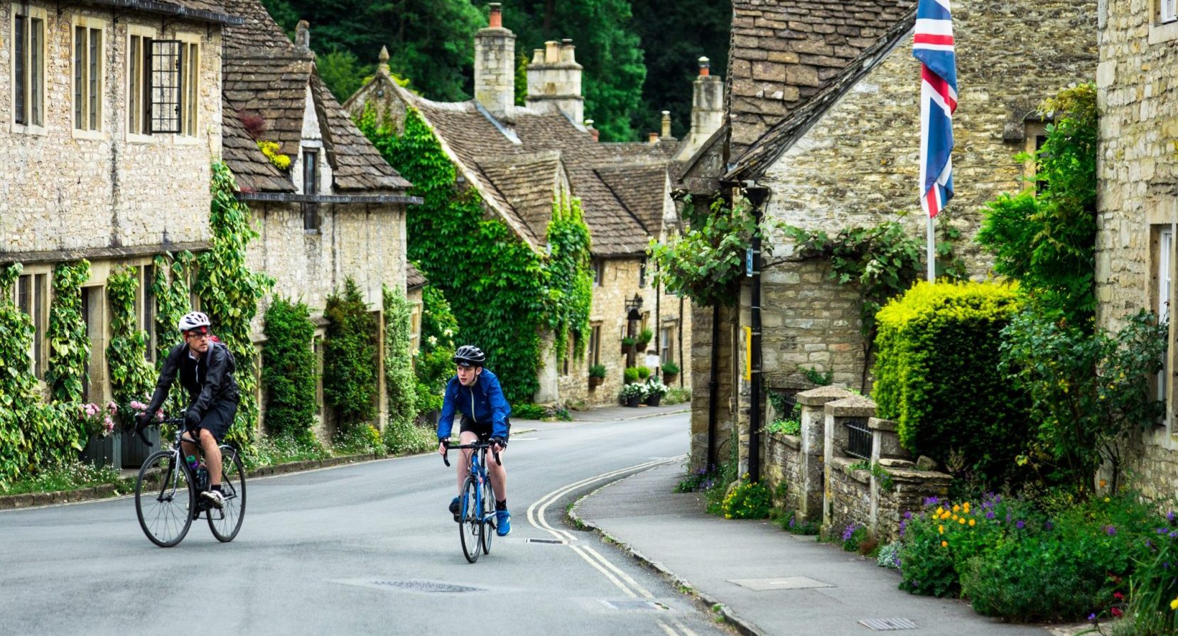 Cyclists riding through traditional English village with cozy cottages